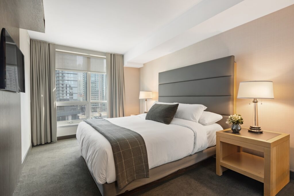 A cozy, well-furnished vacation rental bedroom with warm lighting, quality linens, and natural light